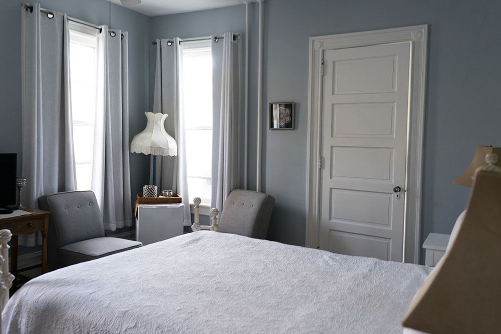 Dorothy Thompson room with blue-gray walls, white bedding and two armchairs