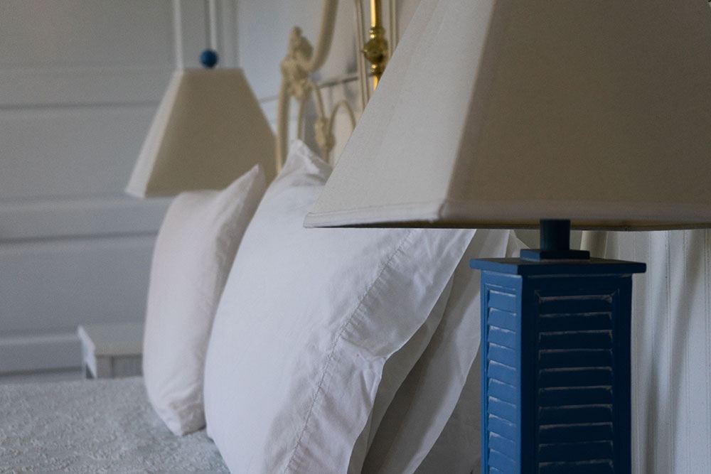Lillian Hastings headboard detail with white pillows and a blue shutter-style lamp