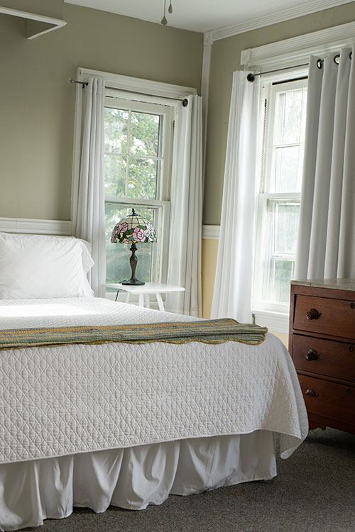 Mary Francis Denning room with white quilted bed, Tiffany-style lamp and two windows