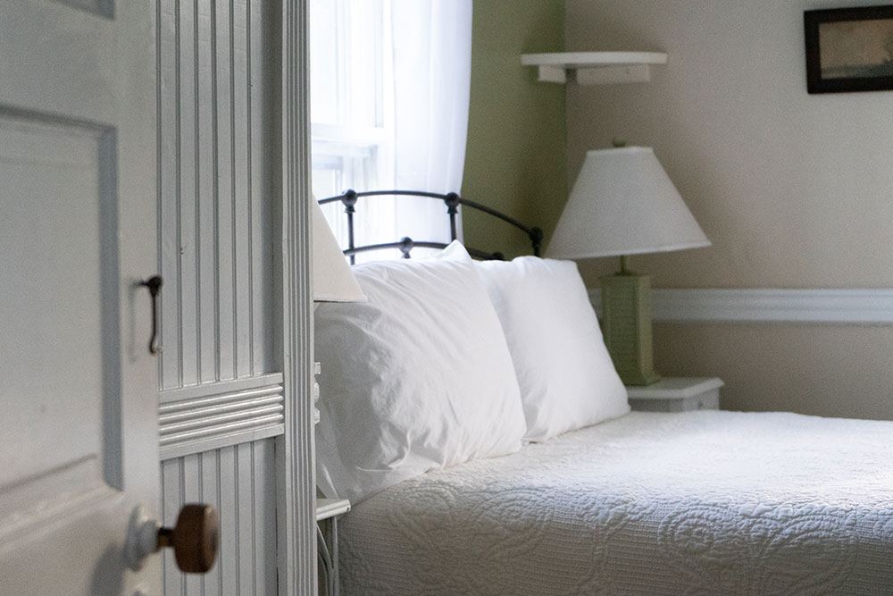 Shannon Room with bed beside the door, white quilted cover and pale green walls