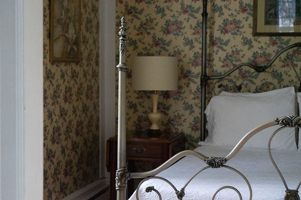 Smith Cottage interior with four-poster iron bed and floral wallpaper